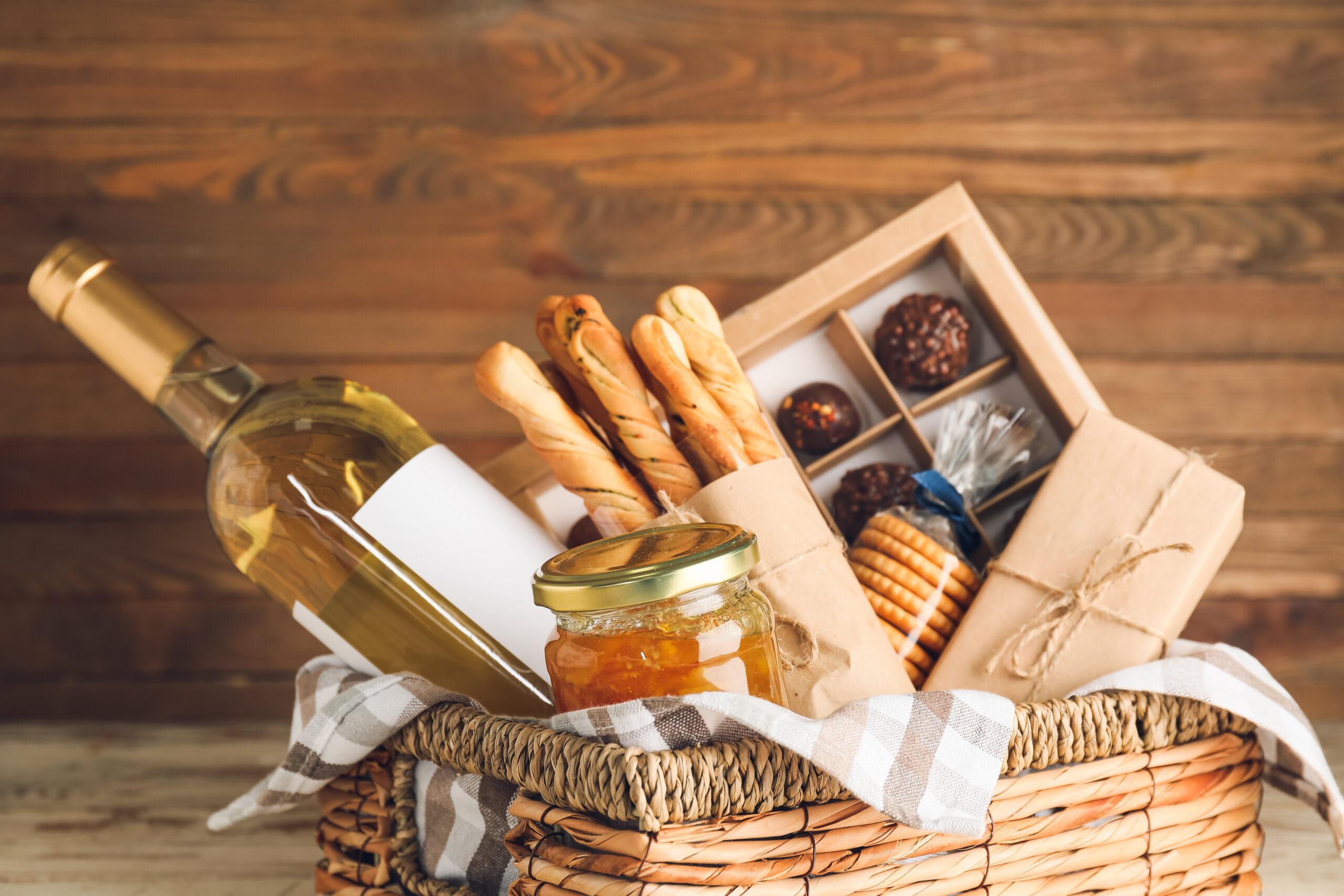 Basket of food with wine, breadsticks, jam, crackers and chocolates to give as gifts for foodies.