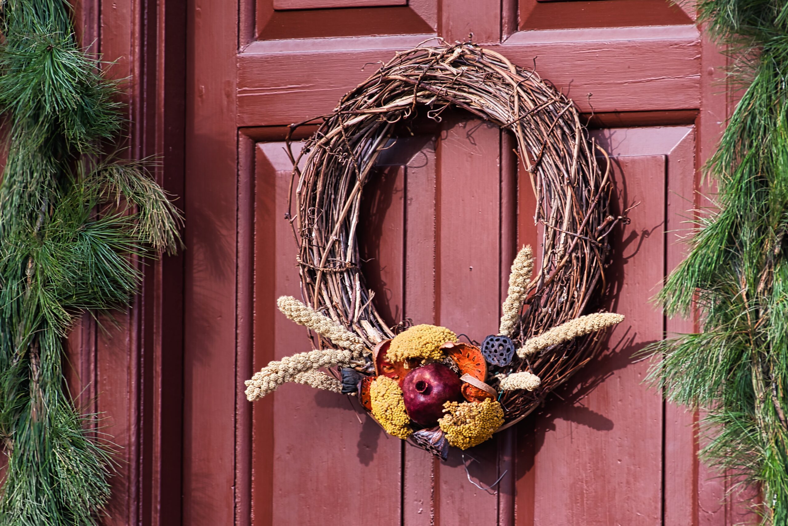 grapevine wreath hanging on a red front door with greenery on the sides of the door